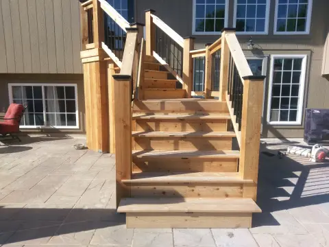 Custom cedar deck stairs with wooden posts and black metal balusters connecting to paver stone patio